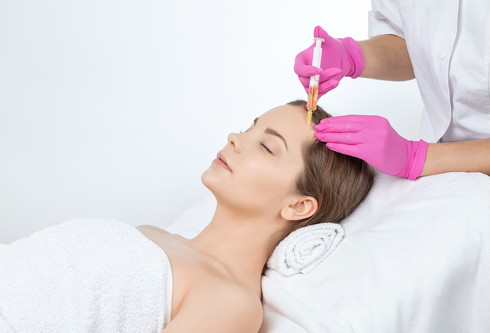 A woman receives PRP (Platelet-Rich Plasma) therapy on her forehead by a medical professional wearing pink gloves.